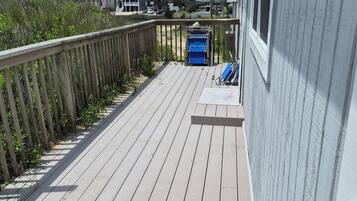 A wooden deck with a railing, a blue trash bin, and a window.