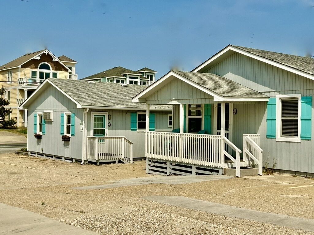 A row of beach houses with white railings and green shutters, featuring a simple, coastal architectural style.