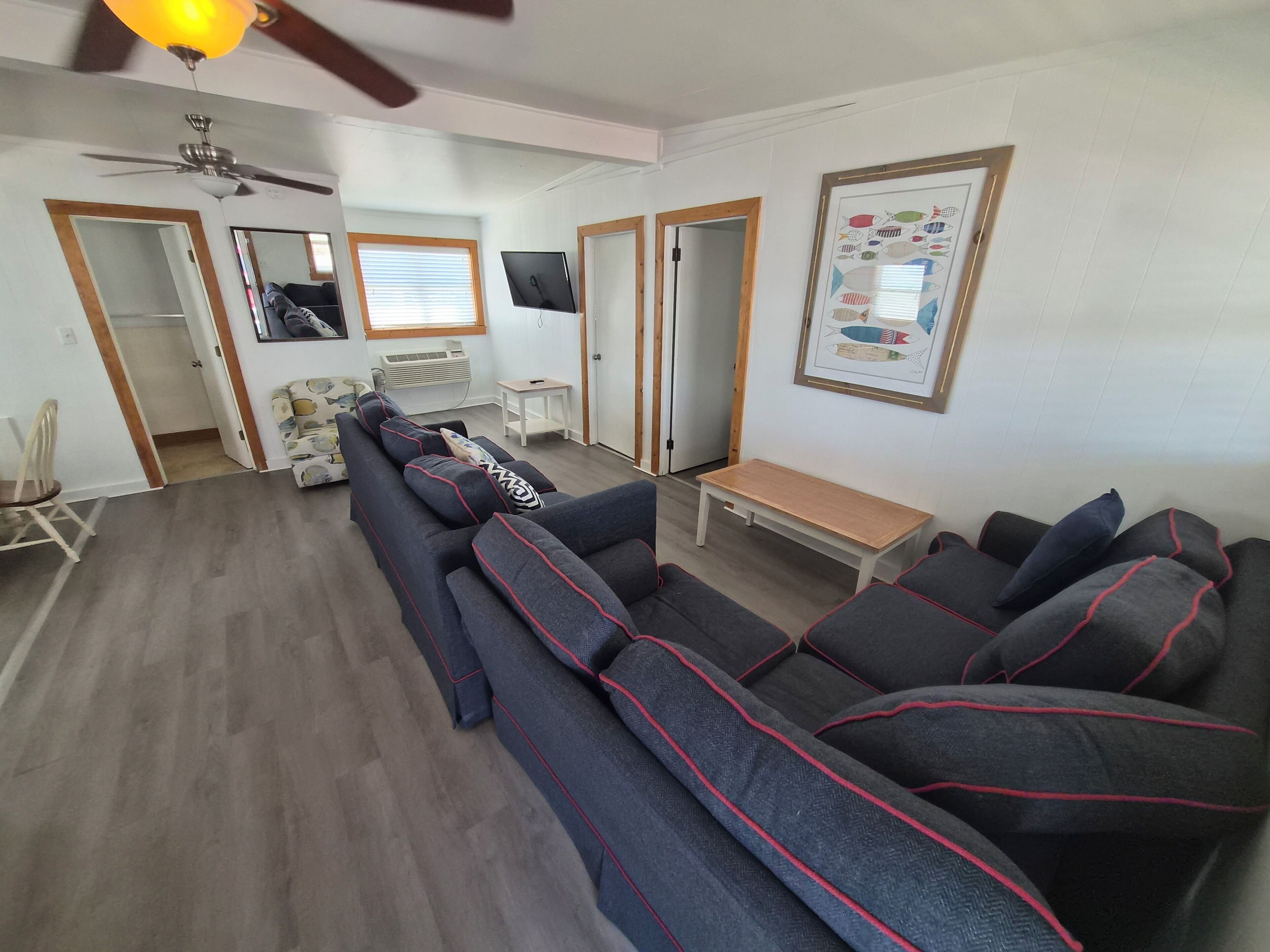 Un salon avec un canapé, une table basse, un ventilateur de plafond et un tableau représentant un poisson, encadré.