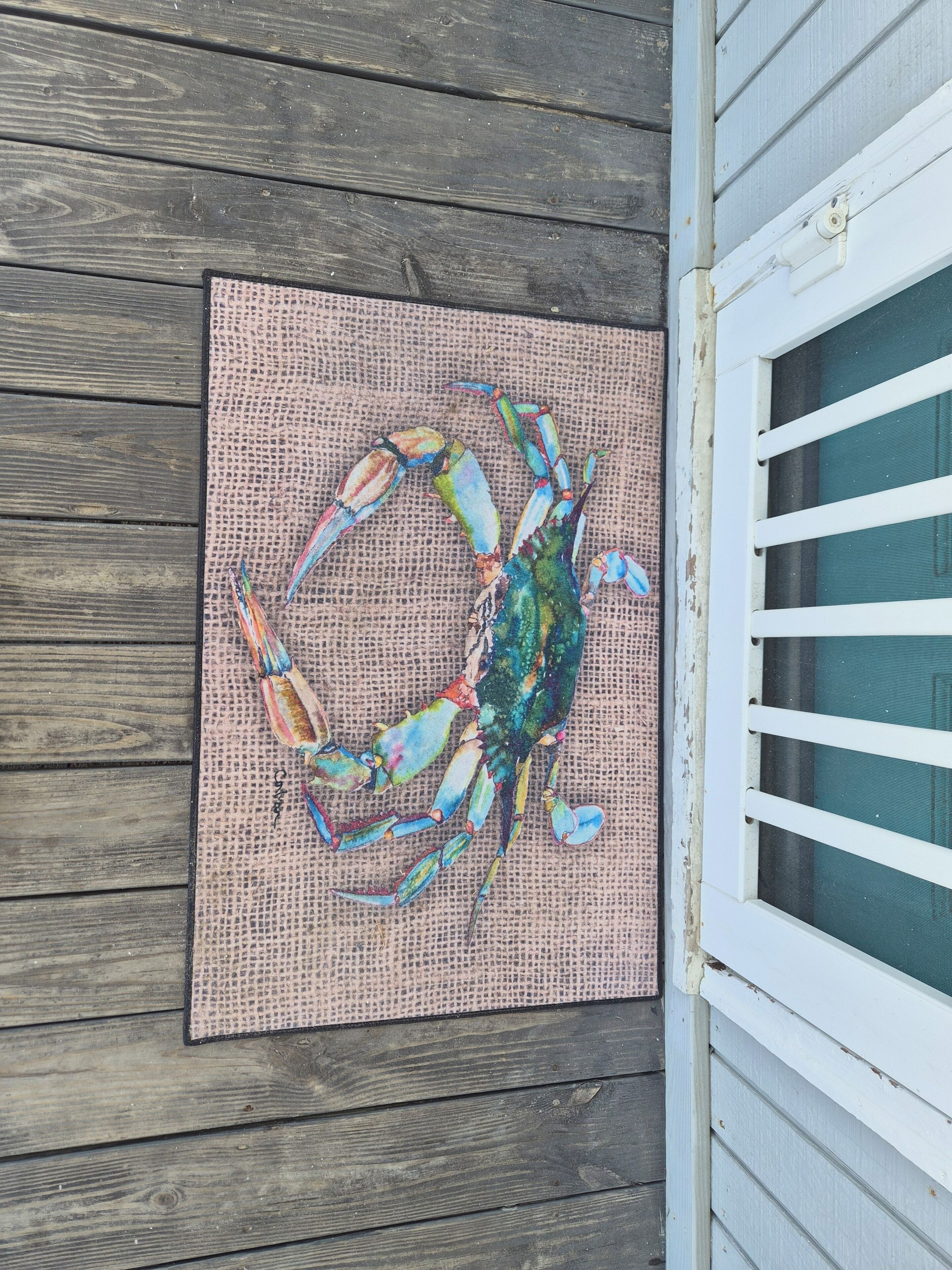 A wooden deck with a woven mat and a colorful crab artwork.