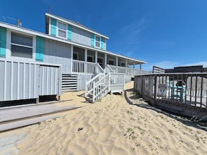 A beachfront building with a wooden deck, a staircase leading to a covered porch, and a sign indicating reserved parking. - SandSpur Ocean Cottages (Nags Head)