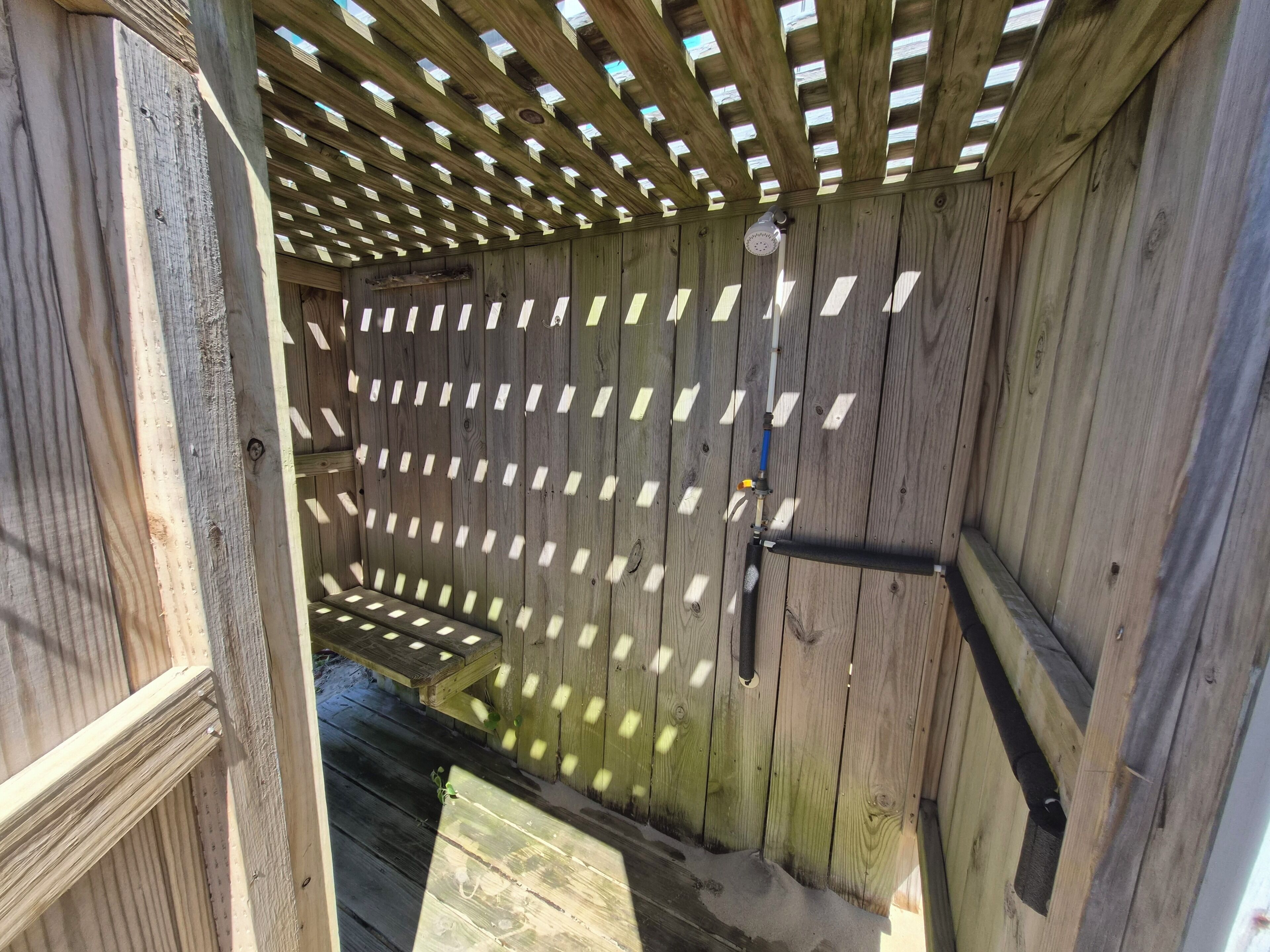 A wooden structure with a slatted ceiling, a metal pipe, and a bench.
