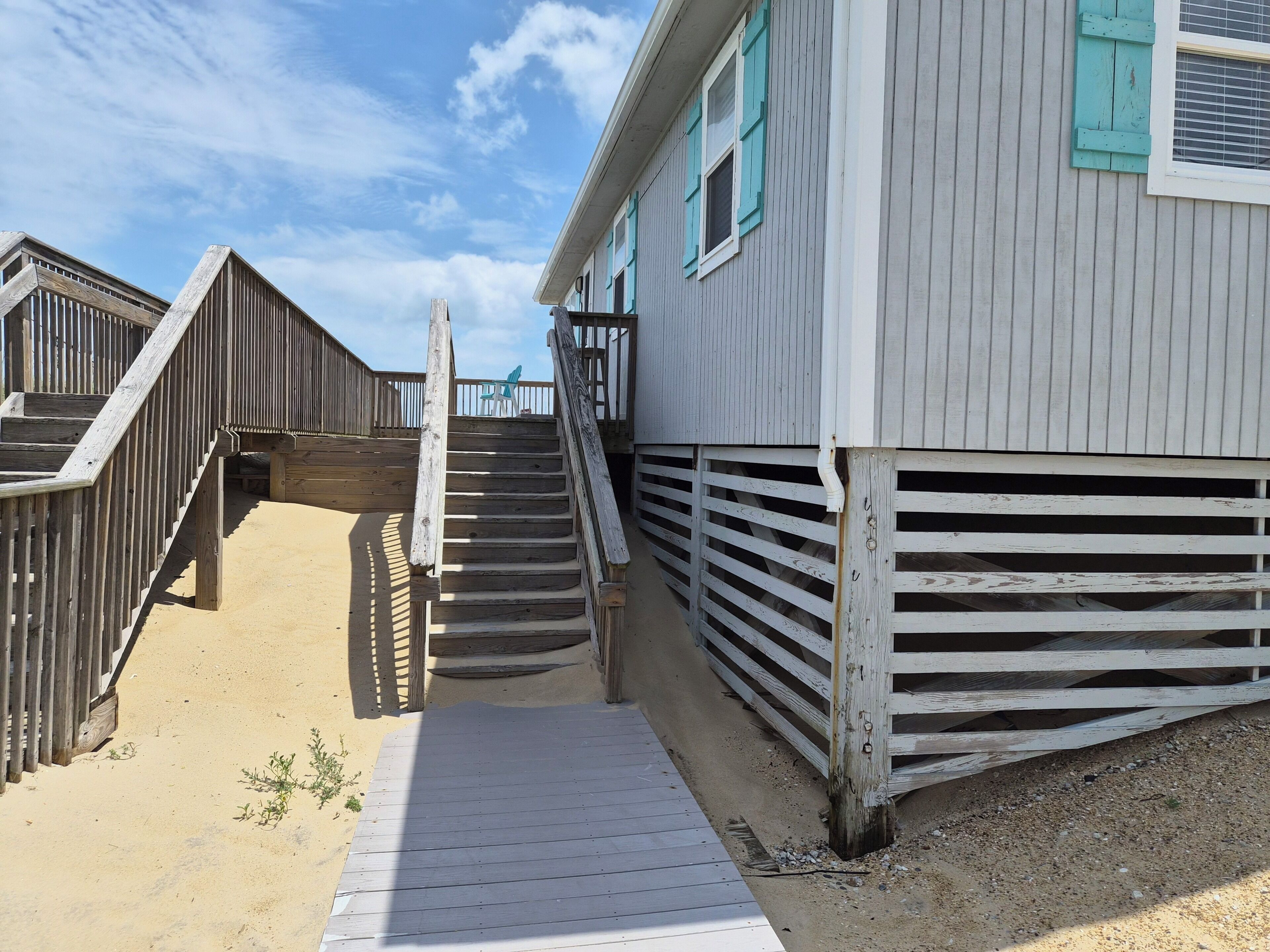 Un escalier en bois mène à un bâtiment dont le sol est recouvert de sable.