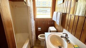 A compact wooden bathroom with a bathtub, toilet, and sink.