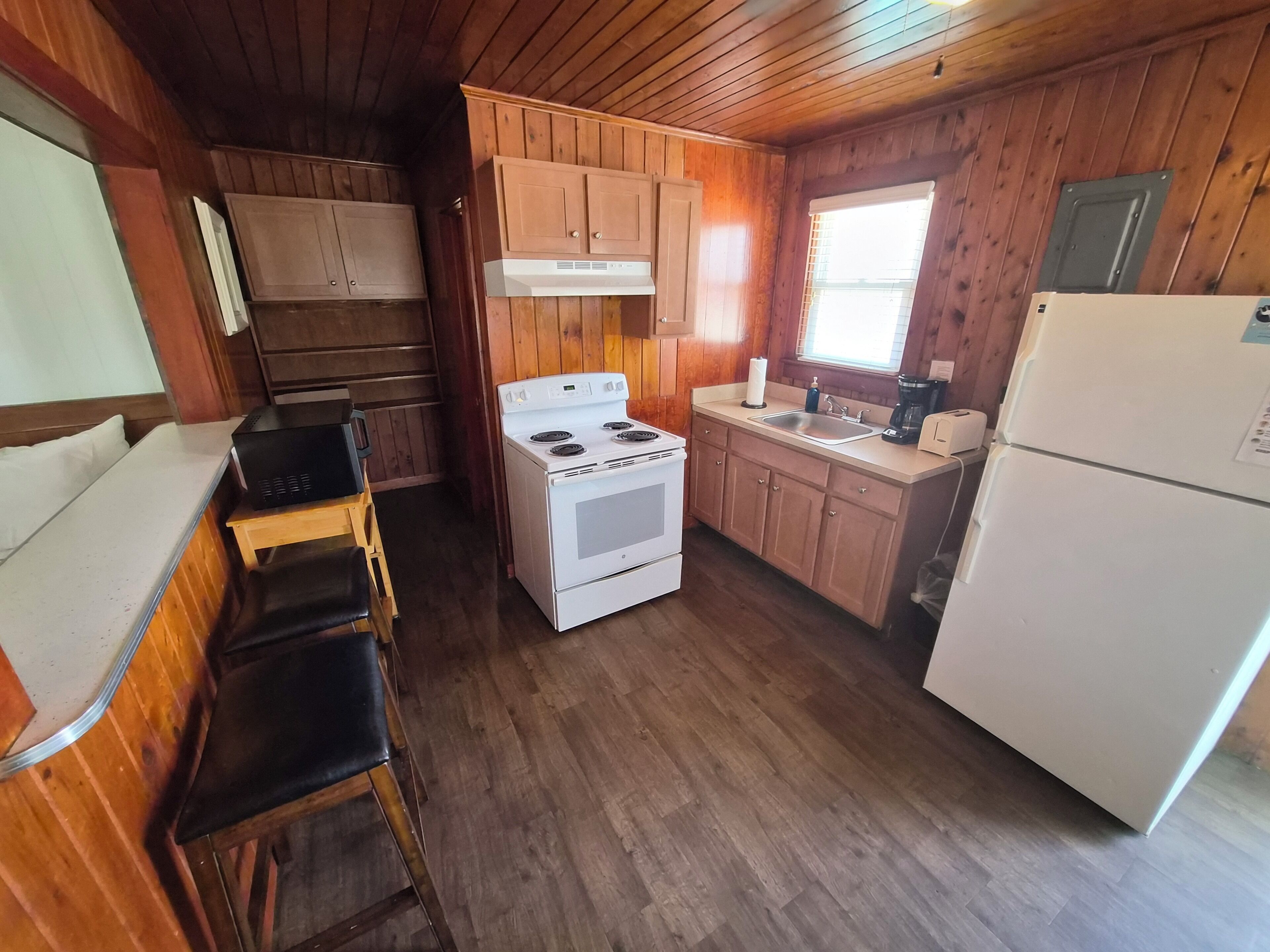 Cocina compacta con armarios de madera, estufa, lavamanos y refrigerador.