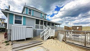 A beachfront house with a wooden deck and a staircase leading to a porch.