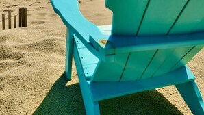 A turquoise beach chair facing the ocean with a sandy beach and a wooden fence in the foreground.