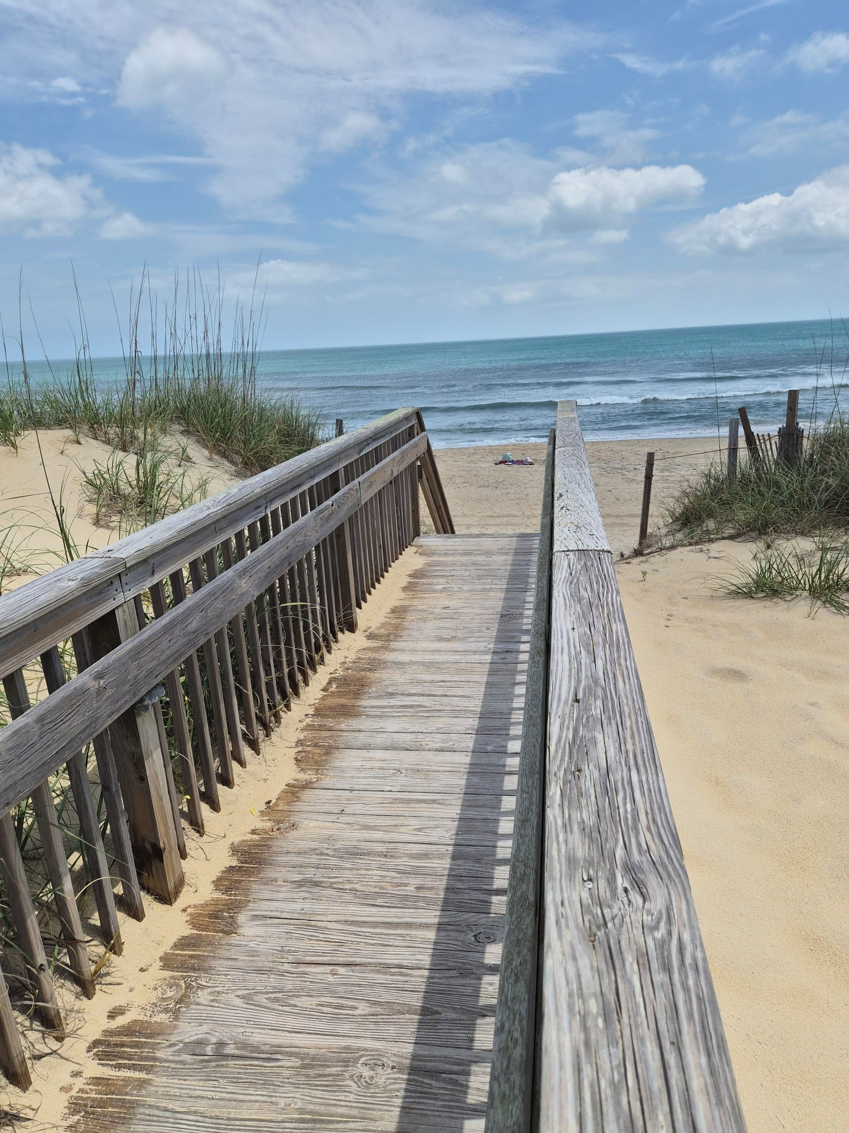 Una passerella in legno conduce a una spiaggia sabbiosa con l'oceano sullo sfondo.