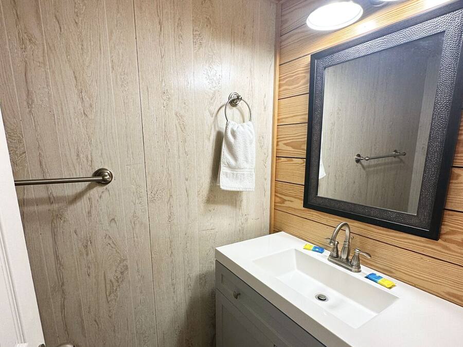 Une salle de bain avec un mur en bois, un lavabo blanc, un miroir et une serviette suspendue à une tringle en métal.