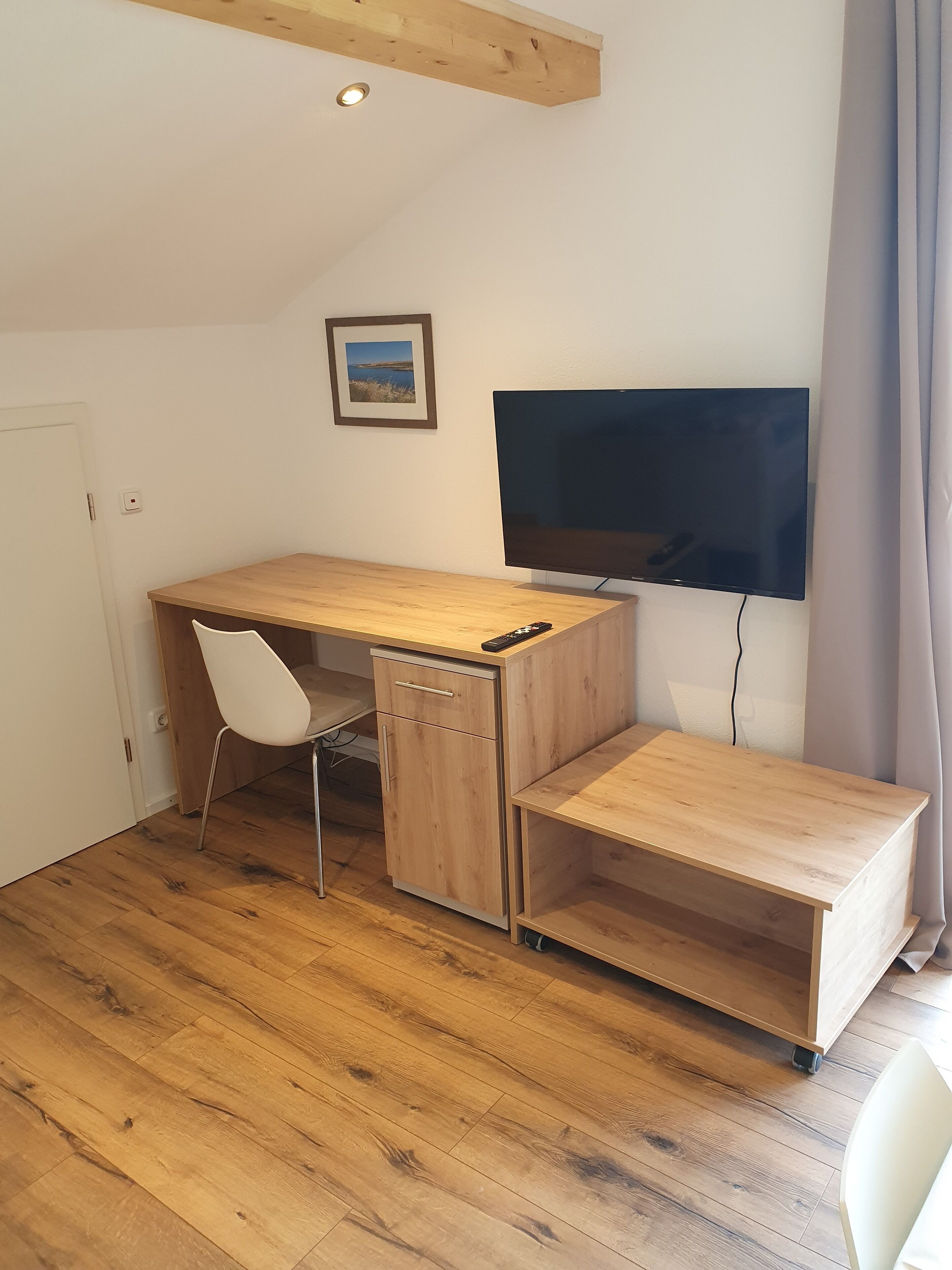 A compact room with a wooden desk, a white chair, a small cabinet, a television, and a door.