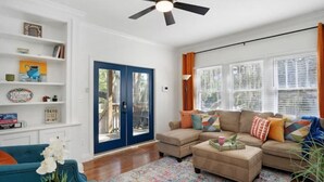 A living room with a sectional sofa, a coffee table, and a ceiling fan. There is a bookshelf with various items and a door leading outside. - Kayak from your backyard (Bradenton)