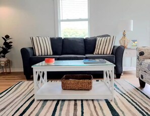 Relax in this inviting living space with a cozy coffee table, plush sofa, and natural light pouring in through the window.
