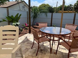 Relax in style with a round table and wicker chairs on this serene patio surrounded by lush greenery and potted plants.