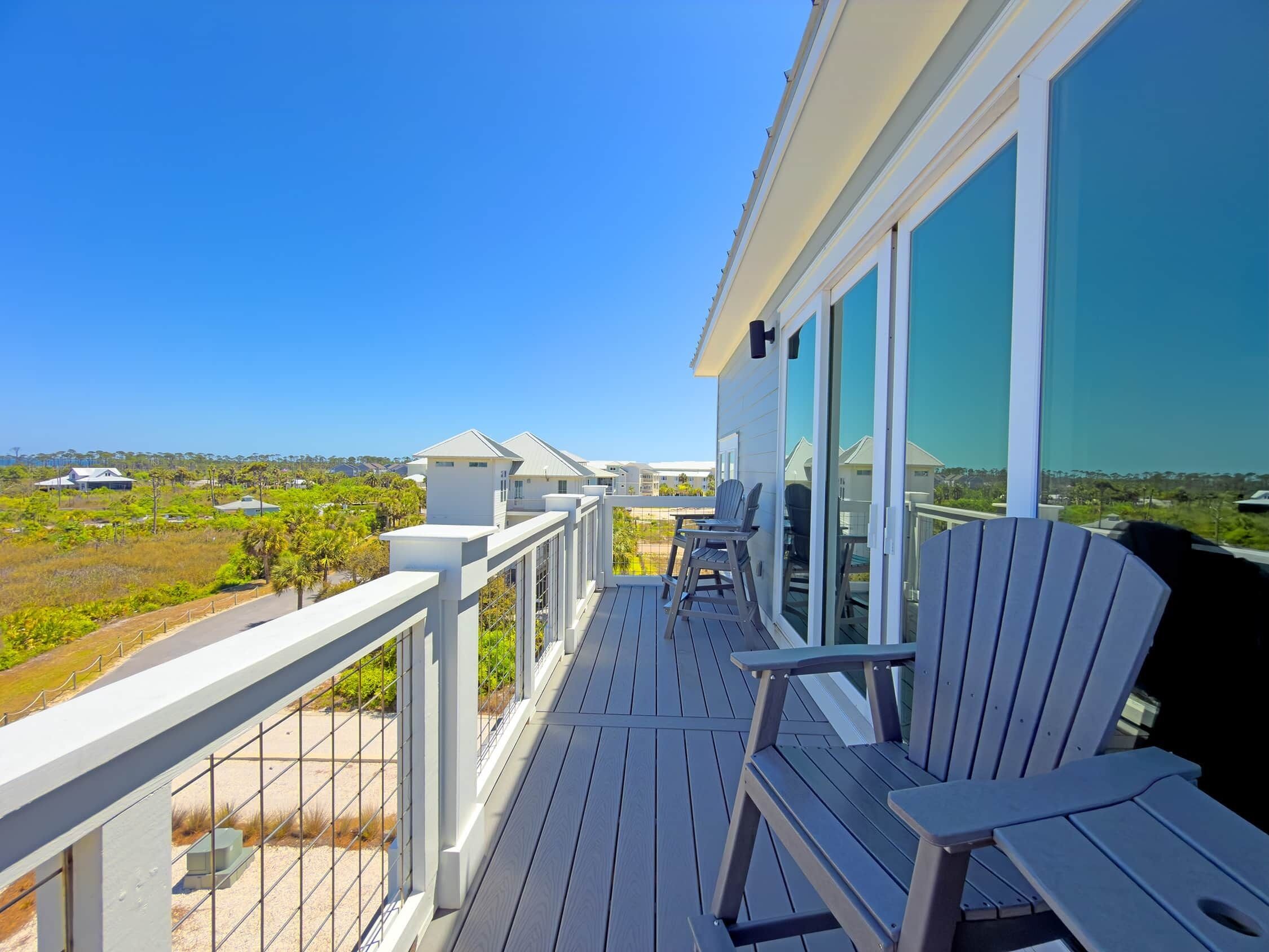 A wooden deck with chairs, a railing, and a view of a residential area.