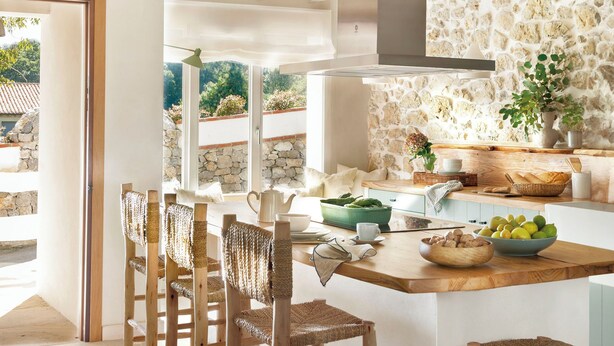 A kitchen with a stone backsplash, wooden chairs, and a large island with fruit and a bowl. - Country House North of Spain (Lamadrid)