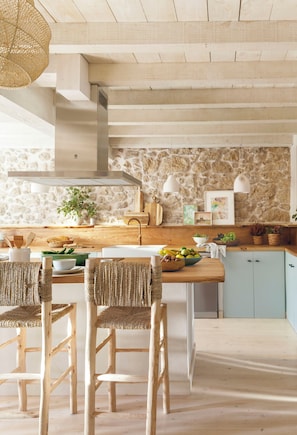Una cocina con pared de piedra, vigas de madera en el techo y una isla central con sillas.