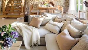 A rustic interior with a stone wall, wooden staircase, and a cozy seating area with cushions and a woven light fixture. - Country House North of Spain (Lamadrid)