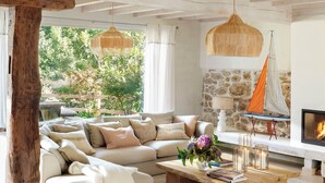 A spacious living room with a large sectional sofa, a wooden coffee table, and a fireplace. There is a stone wall and a view of greenery outside. - Country House North of Spain (Lamadrid)