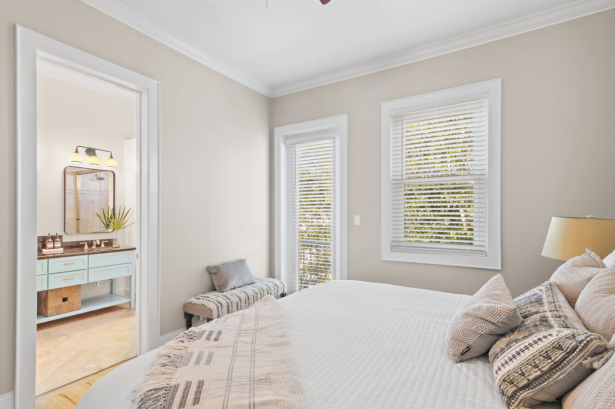 A bedroom with a large bed, a bedside table, a mirror, and a window with blinds.