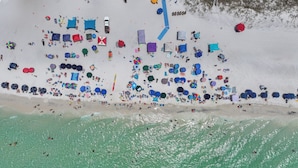 An aerial view of a beach with numerous umbrellas and beach chairs, a clear blue water line, and a sandy beach area. - 30A, 300ft to beach, pool, pingpong, foosball, GulfPlace, ocean views! (Santa Rosa Beach)