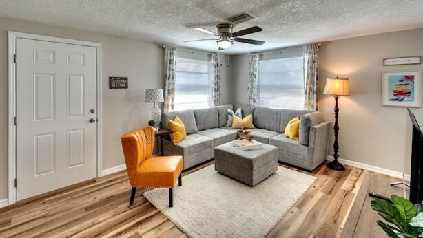A living room with a gray sectional sofa, an orange chair, a white rug, and a ceiling fan.
