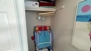 A small room with a bed, a shelf with folded clothes, and a wall-mounted rack with a blue chair.