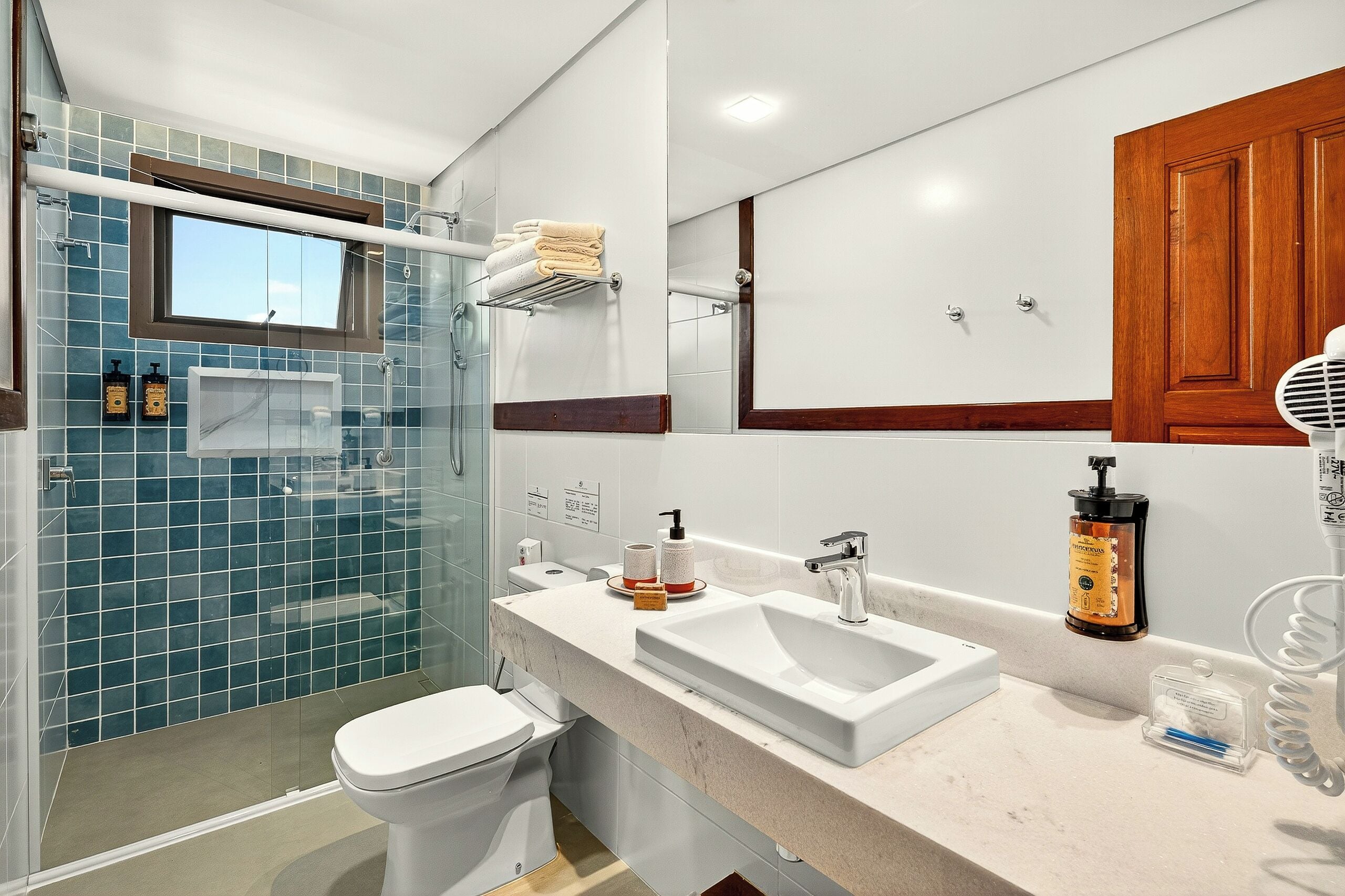 Un baño moderno con cabina de ducha de vidrio, inodoro blanco, lavamanos con espejo y un mueble de madera.