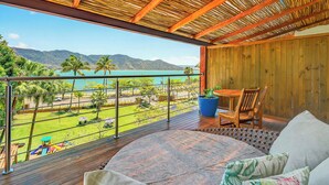 Un balcón con techo de madera, una mesa con sillas y vistas a un paisaje verde y una masa de agua.