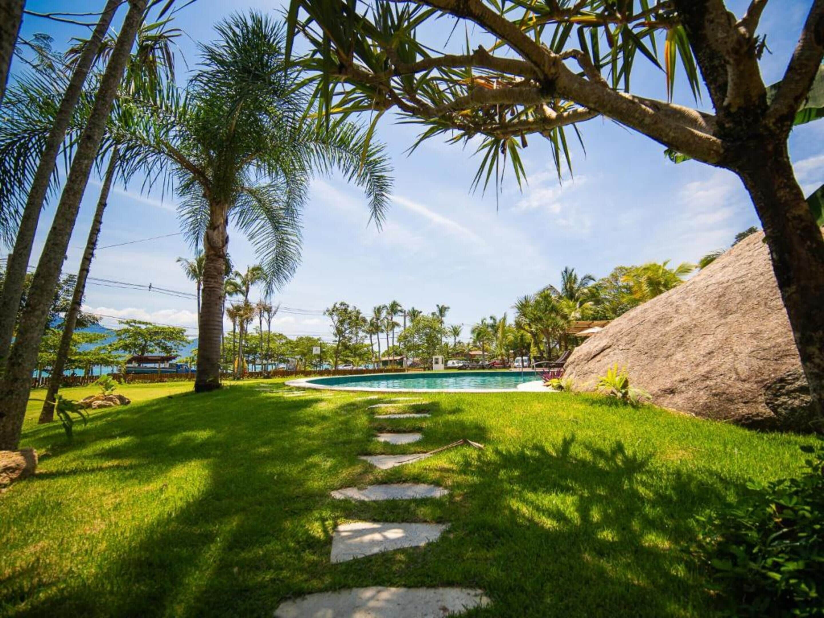 Ein Garten mit Swimmingpool, Palmen und einem großen Felsen.