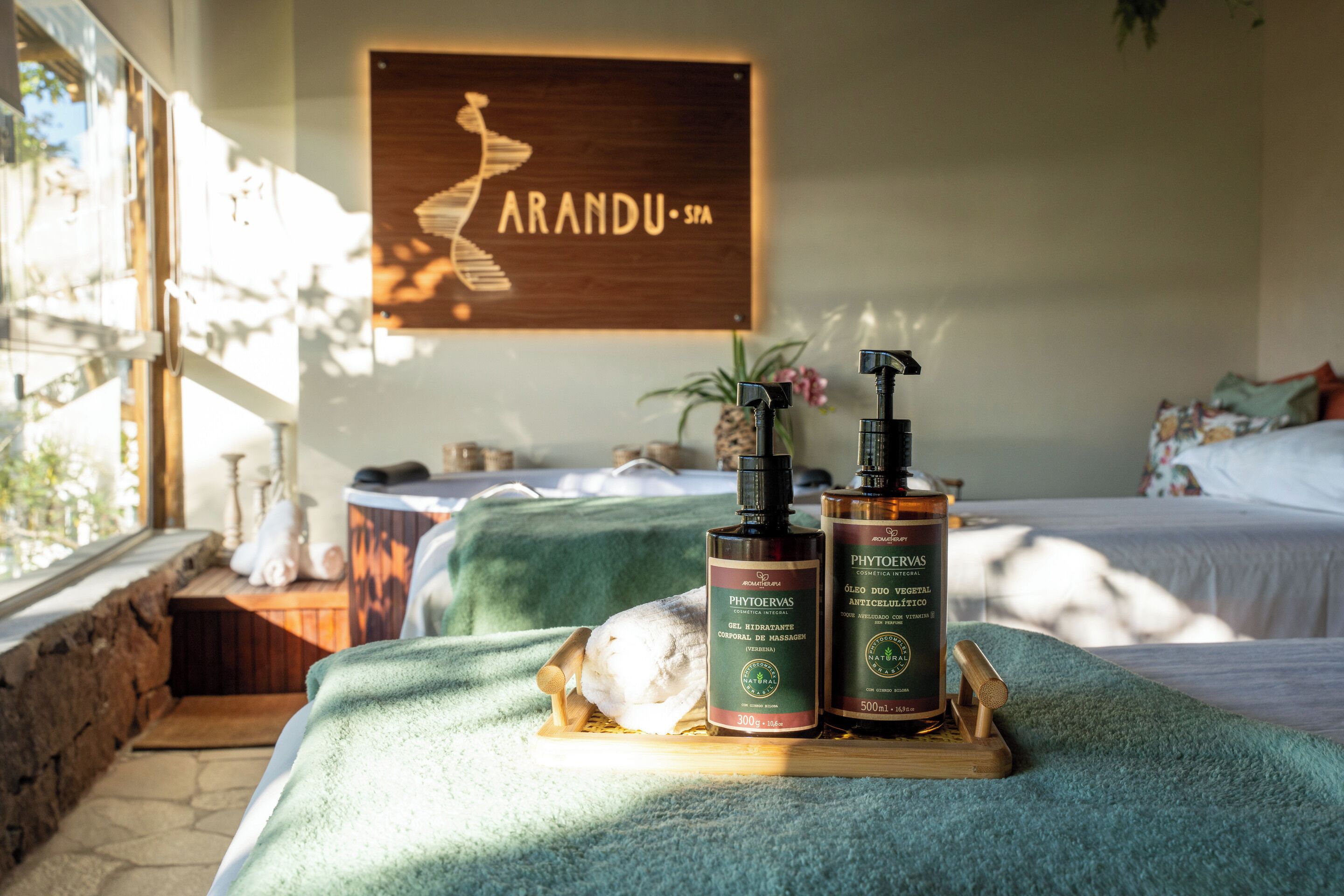 Une salle de spa avec une enseigne en bois indiquant « ARANDU SPA », une table de massage et deux bouteilles de PhytoVas disposées sur un plateau.