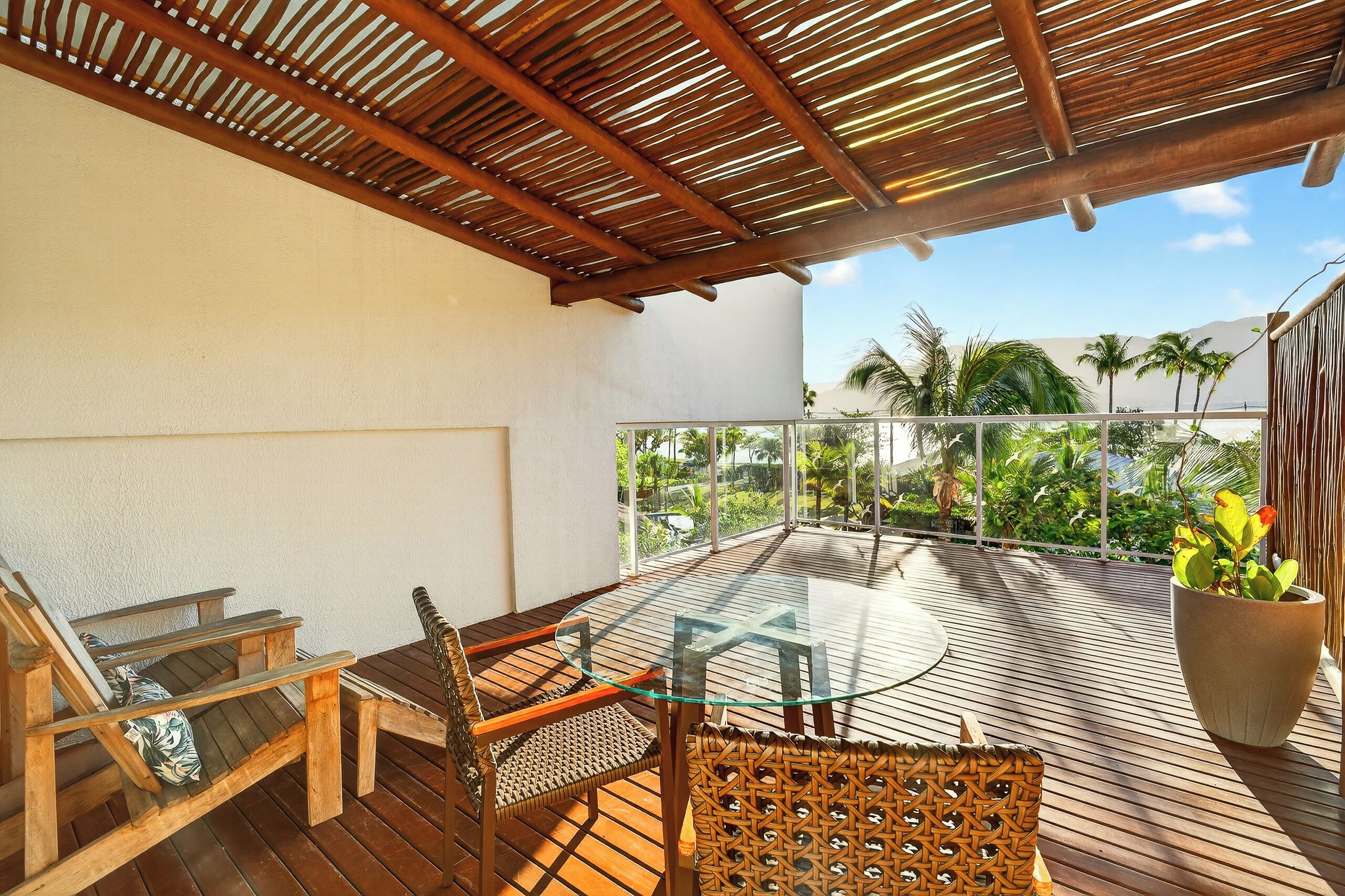 A wooden deck with a glass table and chairs, overlooking a lush garden and a clear sky.