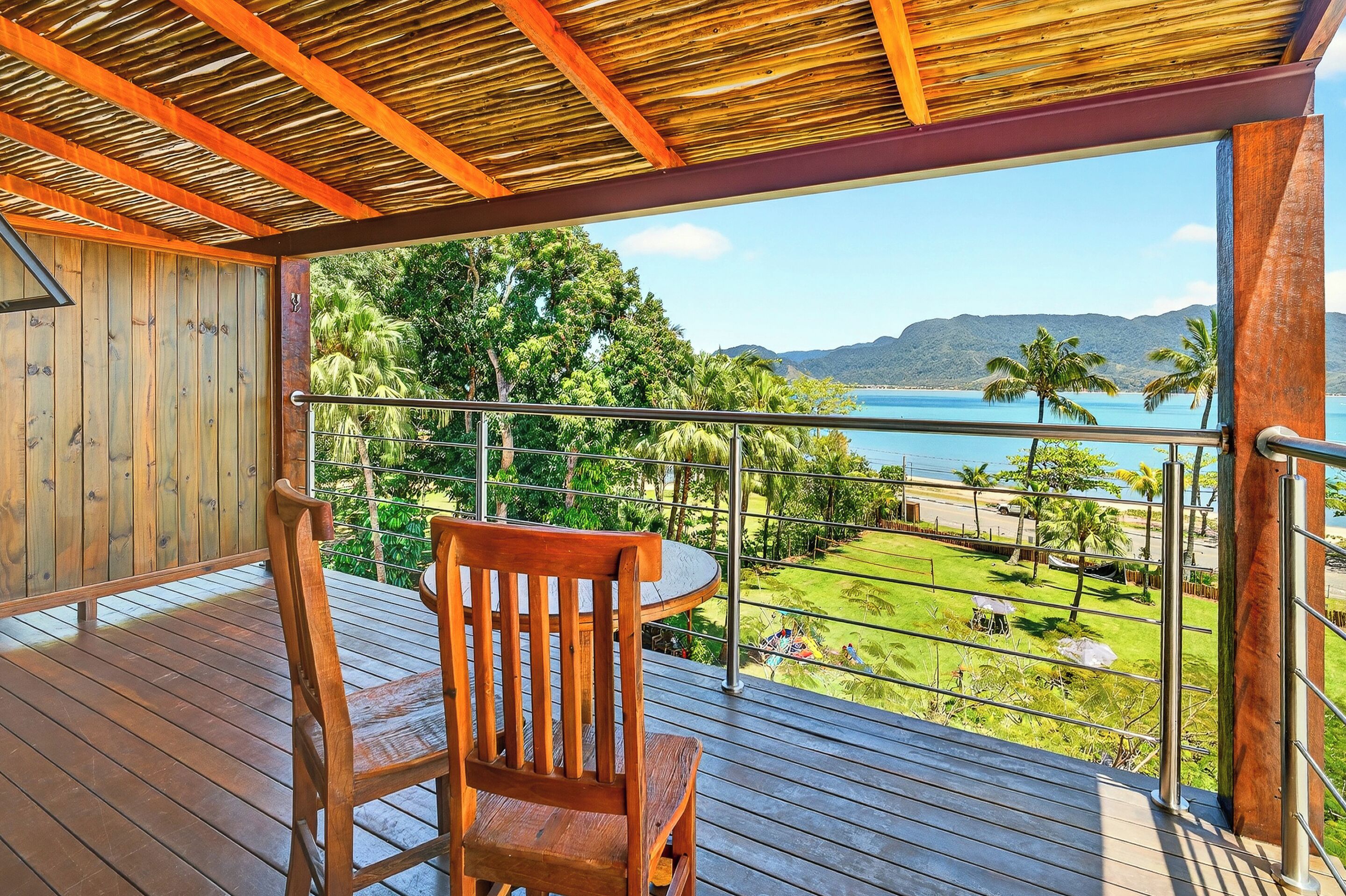A wooden deck with a chair, overlooking a lush landscape with palm trees and a view of the sea.