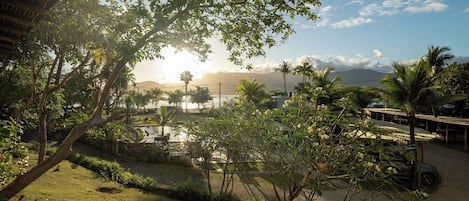 Un jardín arbolado con palmeras, un elemento acuático y vistas a montañas distantes.