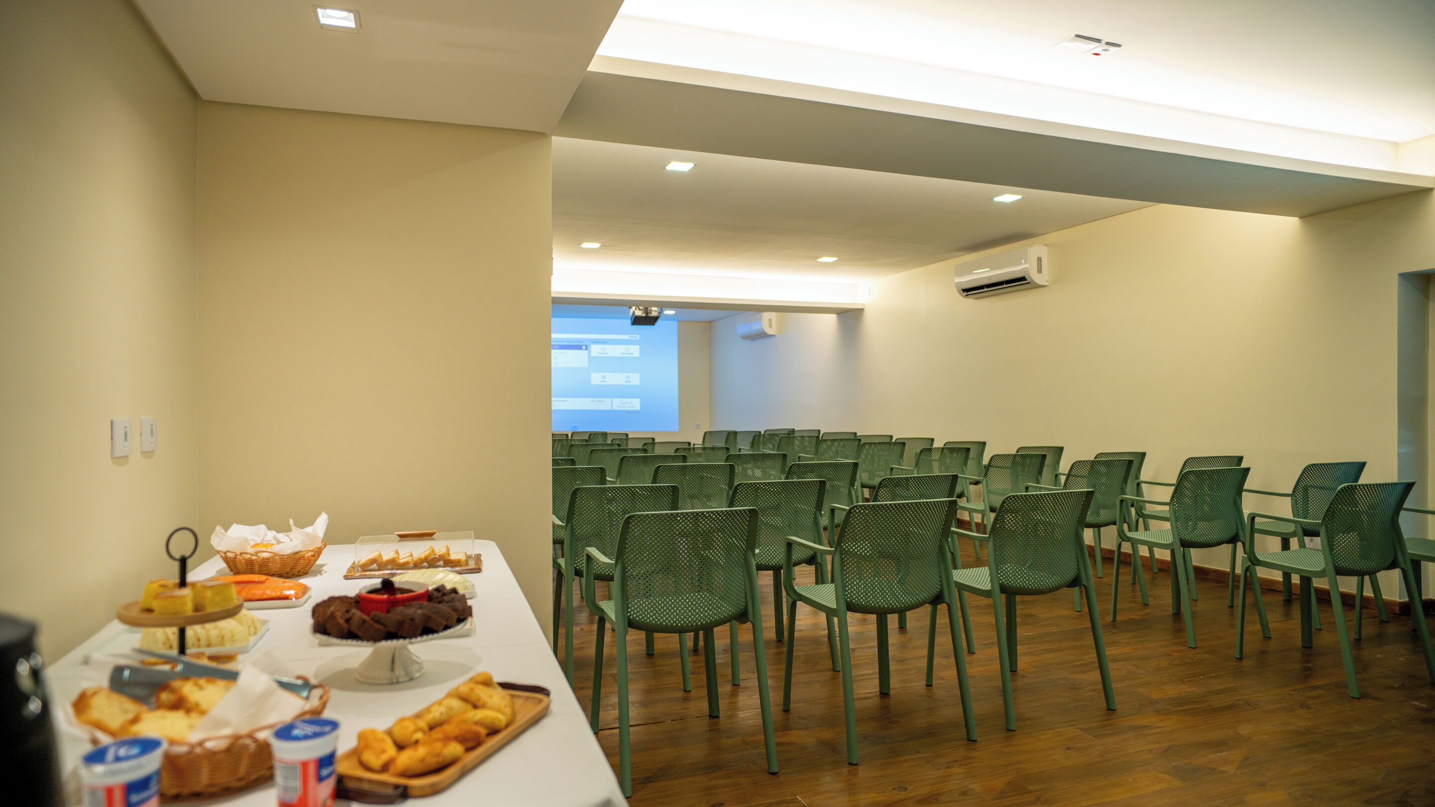 A conference room with rows of green chairs, a buffet table with various food items, and a projector screen in the background.