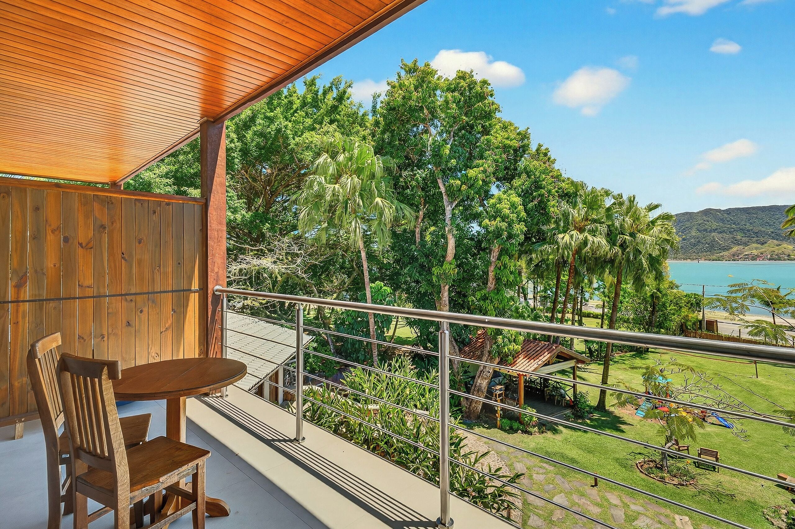 Ein Balkon mit Holztisch und -stühlen, mit Blick auf einen üppigen Garten und ein Gewässer.
