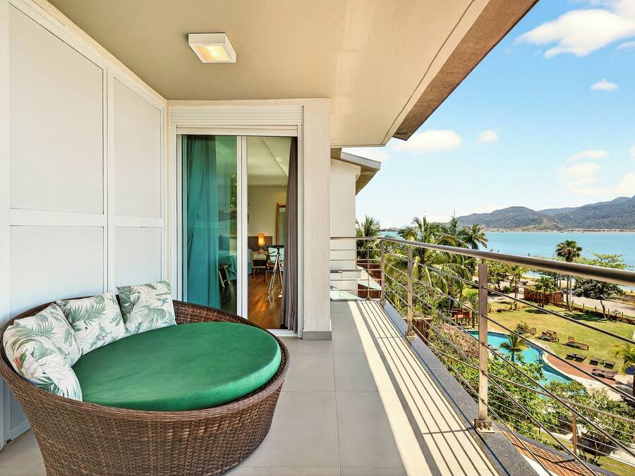 A balcony with a wicker chair and a view of a pool and mountains.