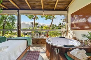 A spa room with a wooden bathtub, a bed, and a view of the landscape. - Velas do Engenho Hotels and Events (Ilhabela)