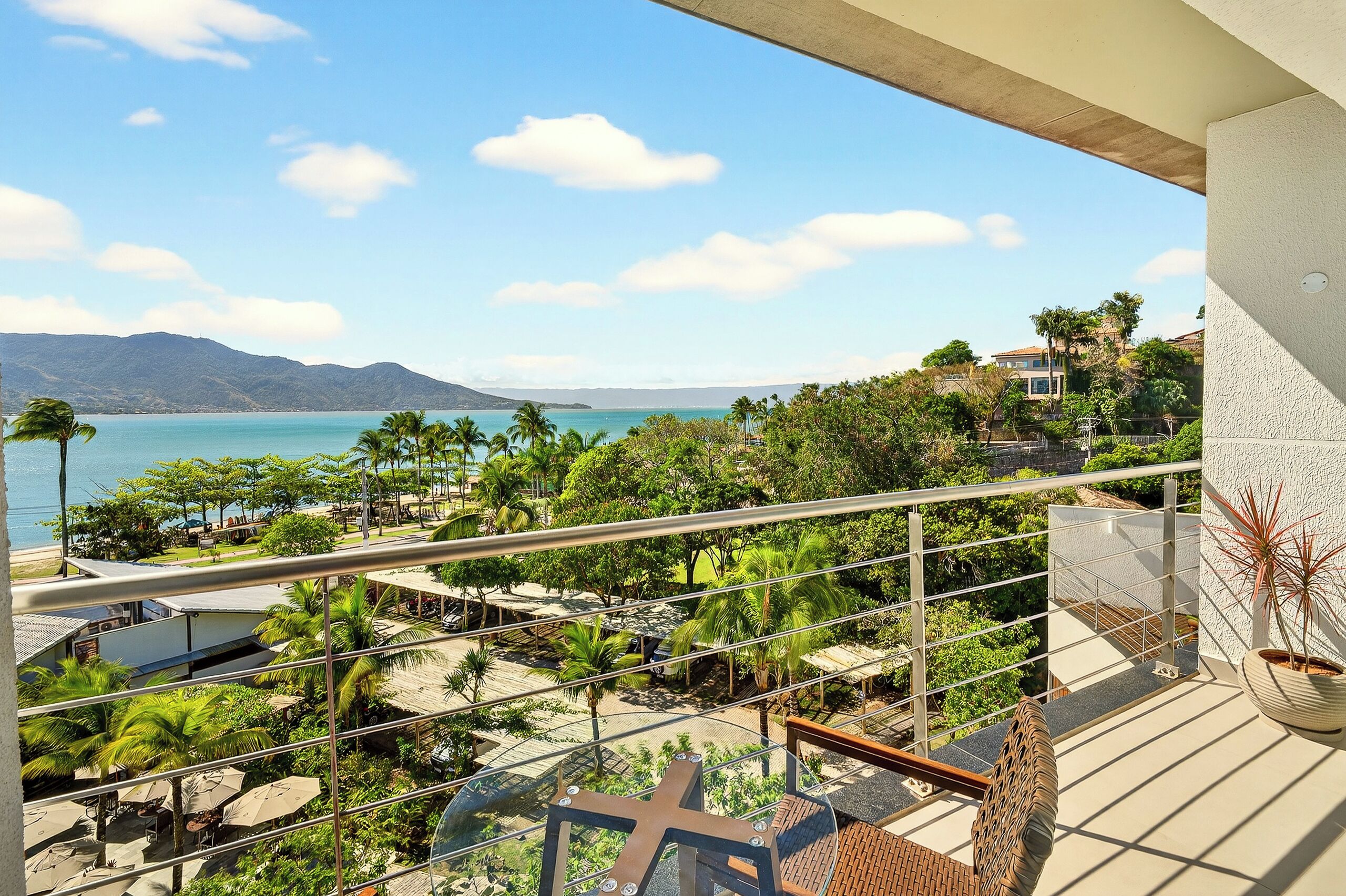 Un balcon avec vue sur une plage, des palmiers et des montagnes.