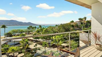Un balcon avec vue sur une plage, des palmiers et des montagnes.