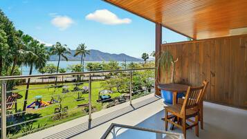 Ein Balkon mit Holzboden, einem Esstisch mit Stühlen und Blick auf einen angelegten Garten und ein Gewässer.