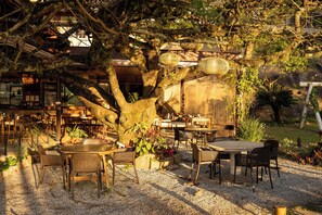 An outdoor seating area with tables and chairs, surrounded by trees and plants.