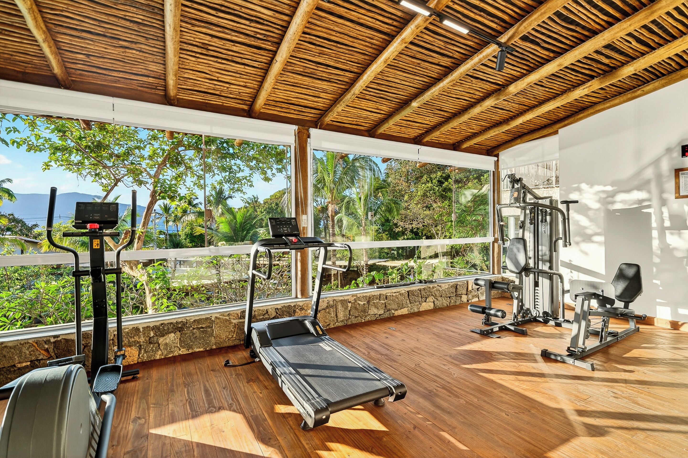 A gym with exercise equipment, a treadmill, and a view of greenery and mountains.