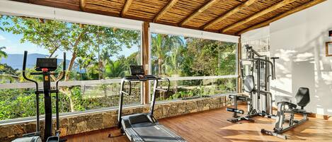 A gym with exercise equipment, a treadmill, and a view of greenery and mountains.