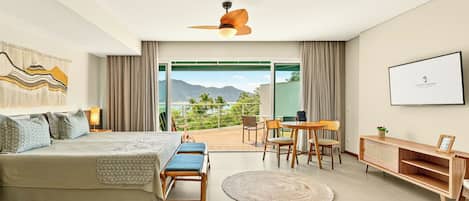 A bedroom with a bed, bedside tables, a desk, and a chair. There is a large window with a view of mountains and a balcony.