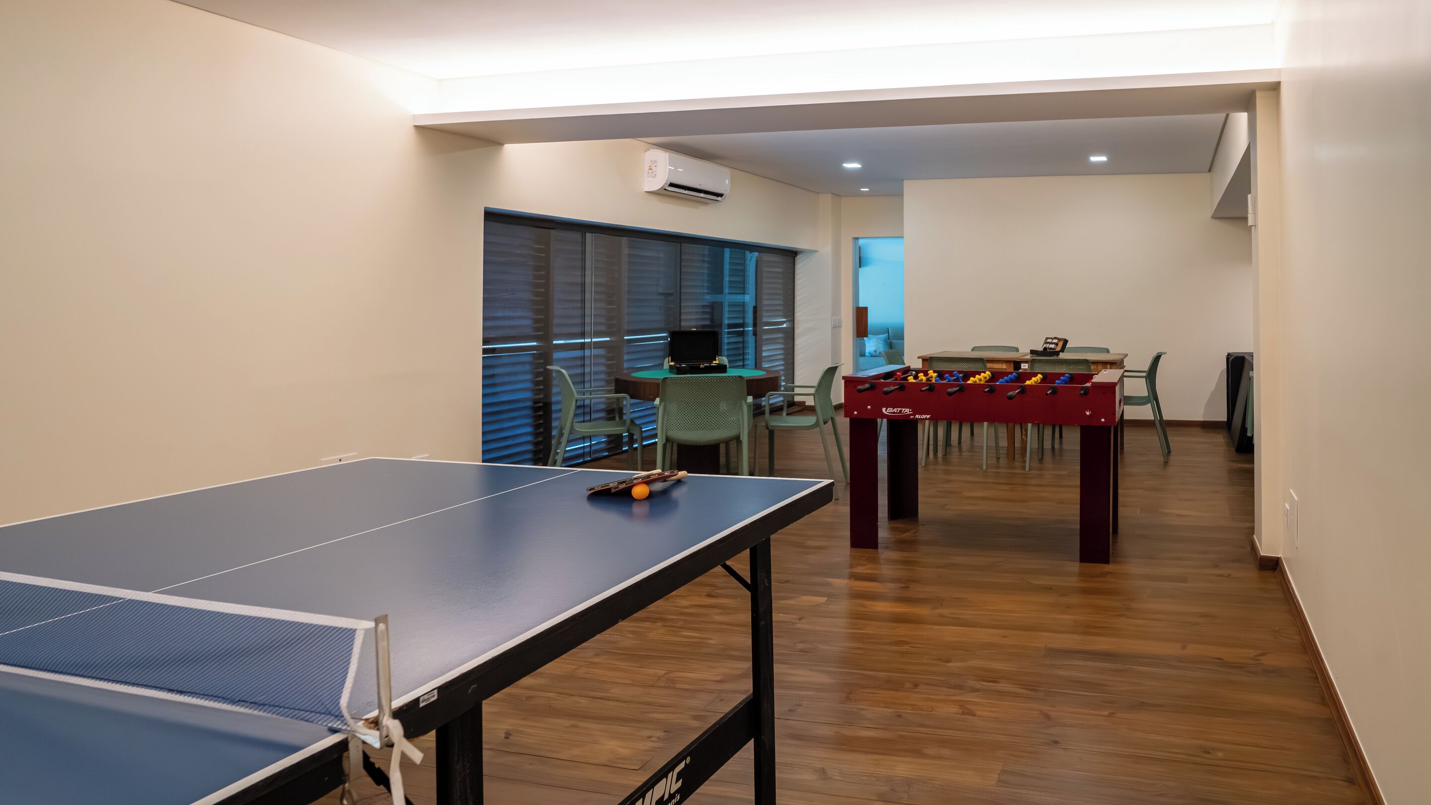 Una habitación con mesa de ping pong, mesa de futbolín y escritorio con computadora.