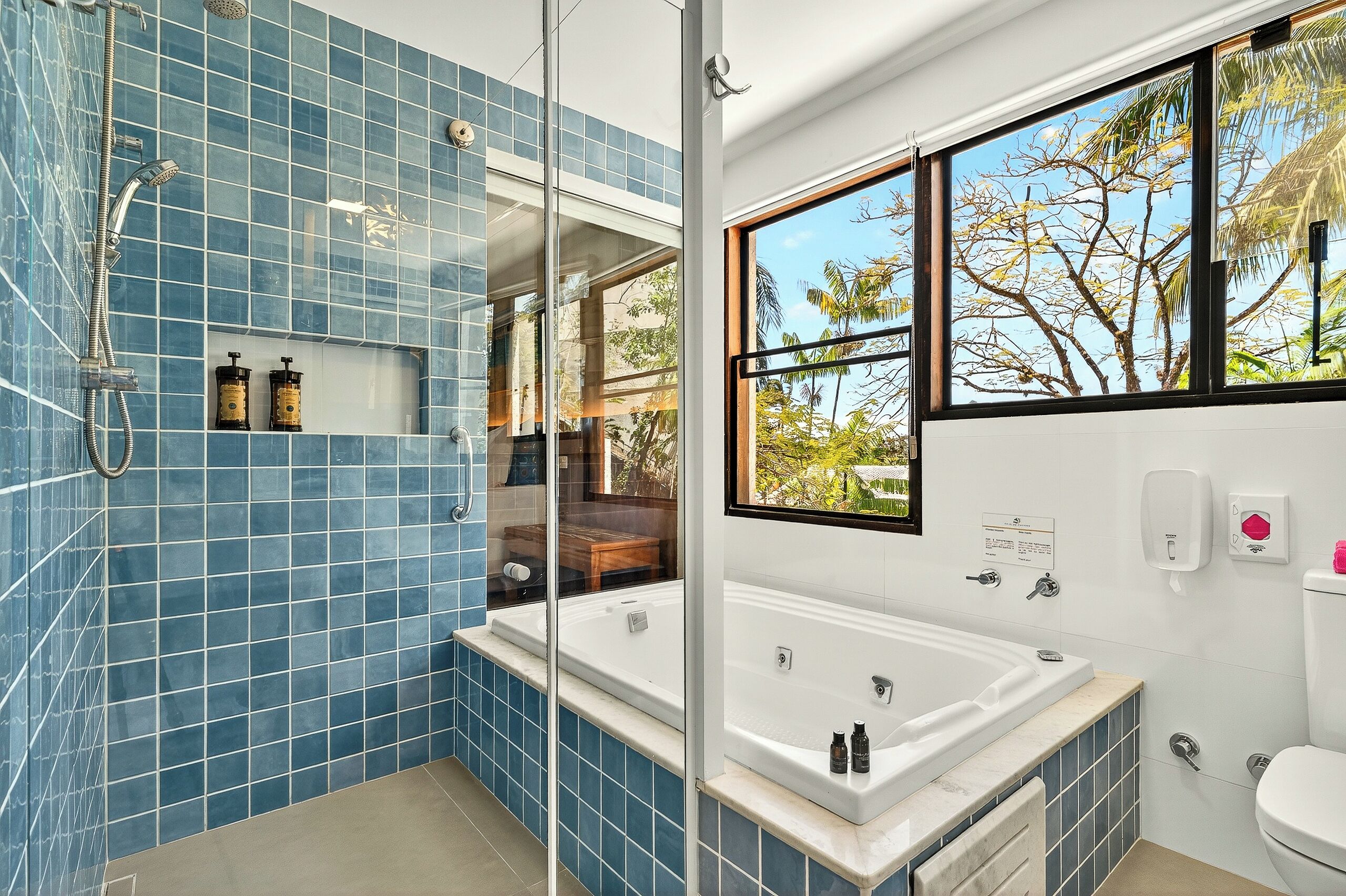 A modern bathroom with a large bathtub, a glass shower enclosure, and a window offering a view of trees.