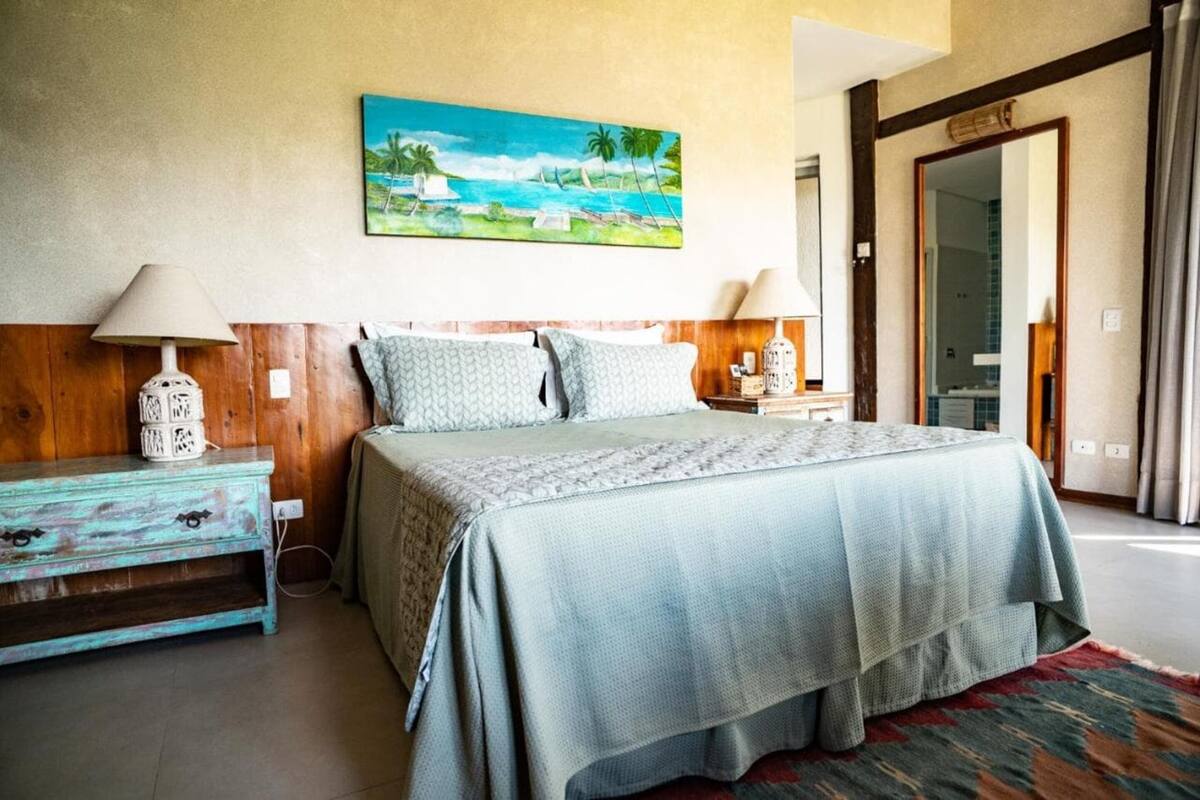 A bedroom with a bed, two nightstands, a lamp, a painting, and a wooden headboard.