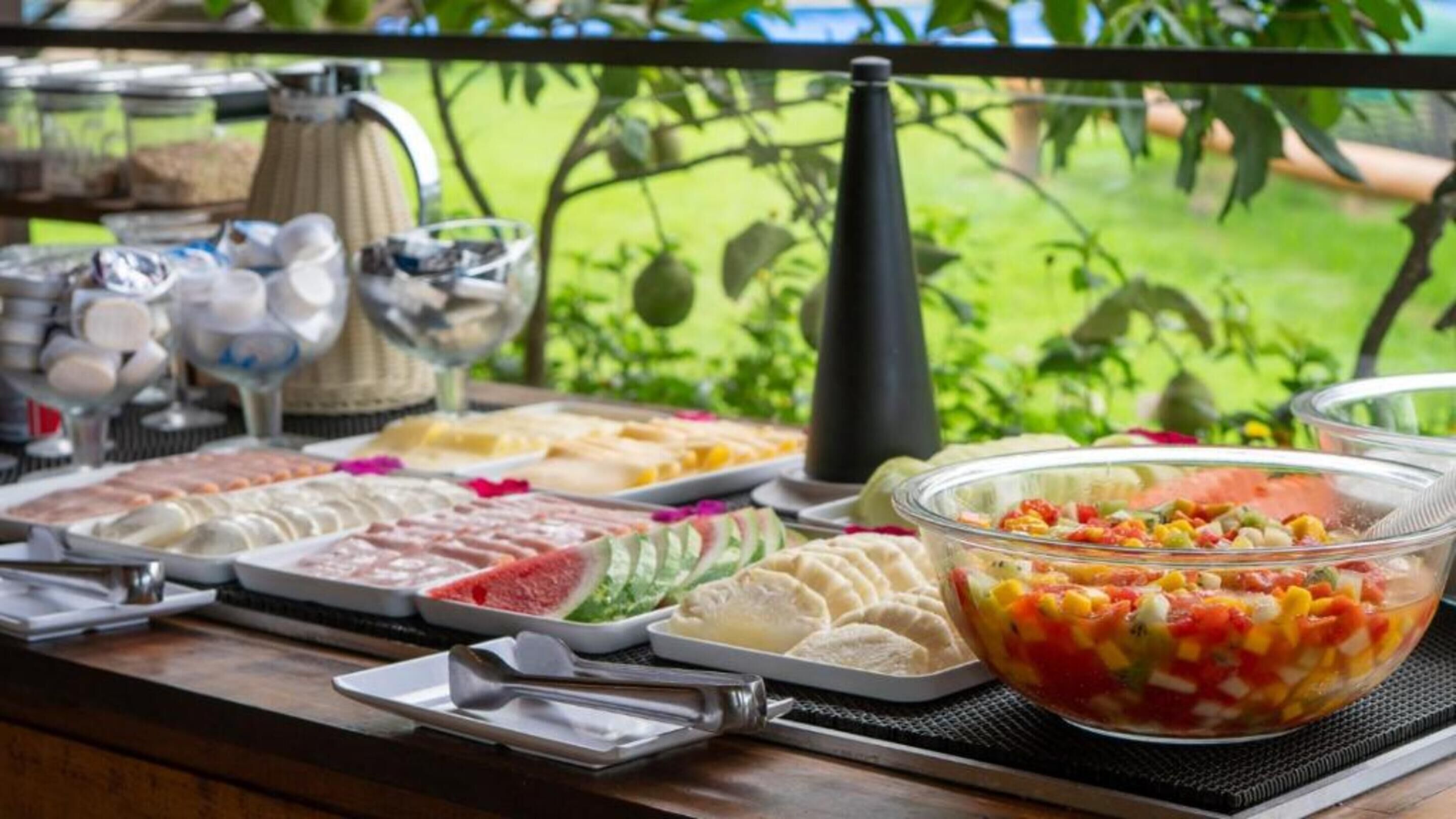 A buffet table with various food items and a clear view of greenery outside.