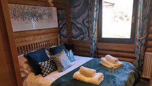 Una habitación tipo cabaña de madera con una cama, almohadas y un ventanal con cortinas.