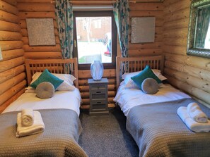 A log cabin room with two beds, each with a pillow and a rolled towel. - Starlight Log Cabin - With Hot Tub and Lake View (Morpeth)